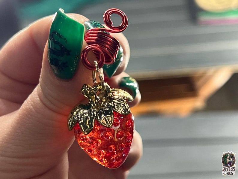 A hand holding a decorative strawberry charm with a red spiral design.