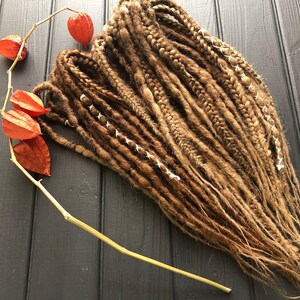 a collection of braided hair strands arranged on a wooden surface, with a few dried orange flowers nearby.