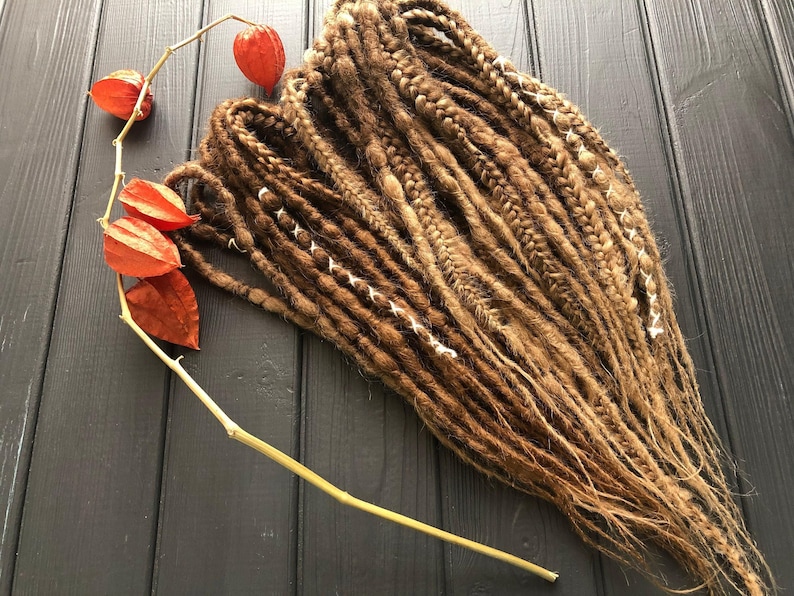 a collection of braided hair strands arranged on a wooden surface, with a few dried orange flowers nearby.