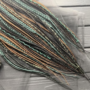 a collection of braided hair strands in various colors, including green, brown, and black, arranged on a wooden surface.