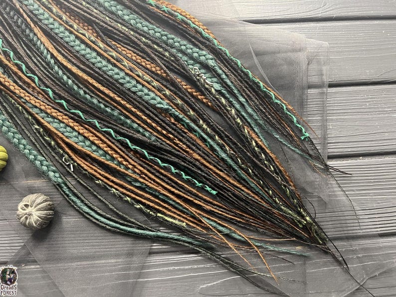 a collection of braided hair strands in various colors, including green, brown, and black, arranged on a wooden surface.