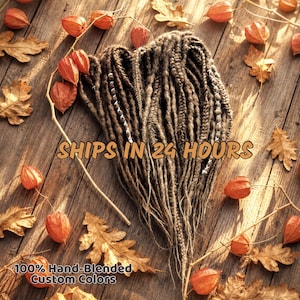 a collection of hand-blended custom hair colors, including various shades of brown and orange, arranged on a wooden surface with autumn leaves scattered around.