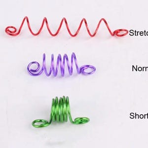 three different types of coiled wire: a red spiral, a purple spiral, and a green spiral. The image is labeled with the words "Stretched", "Normal", and "Shorten" to indicate the state of the coils.