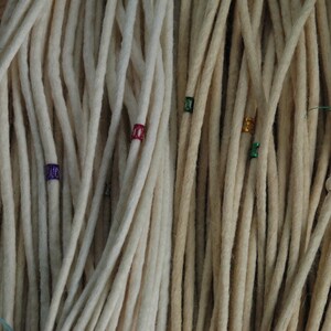 May include: Two sets of white synthetic dreadlocks with colorful beads. The dreadlocks are arranged in a bundle and are ready to be added to hair.