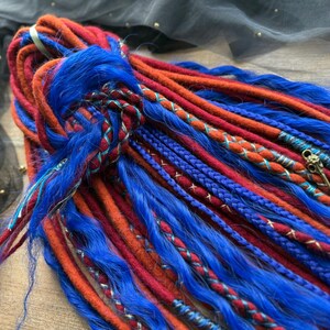 May include: A collection of vibrant dreadlocks in shades of blue, red, and orange. The dreads are intricately styled with braided accents and decorative elements. The image showcases a close-up view of the colorful, textured hair extensions.