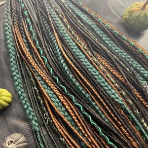 a variety of braided hairstyles, including braids in different colors and patterns, arranged on a wooden surface. There are also some small objects, such as a pumpkin and a small bird, placed alongside the braids.