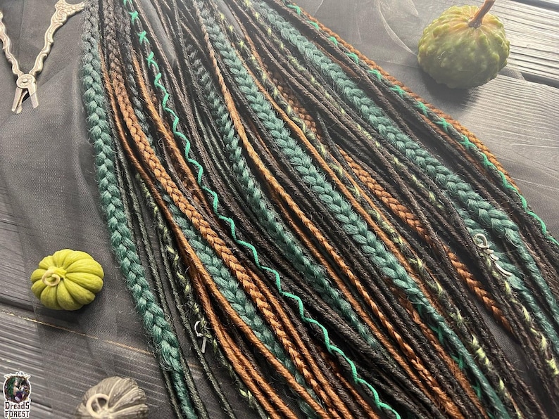 a variety of braided hairstyles, including braids in different colors and patterns, arranged on a wooden surface. There are also some small objects, such as a pumpkin and a small bird, placed alongside the braids.