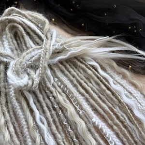 a close-up view of a pile of various colored and styled hair braids or dreadlocks, with a black fabric or sheer material in the background.