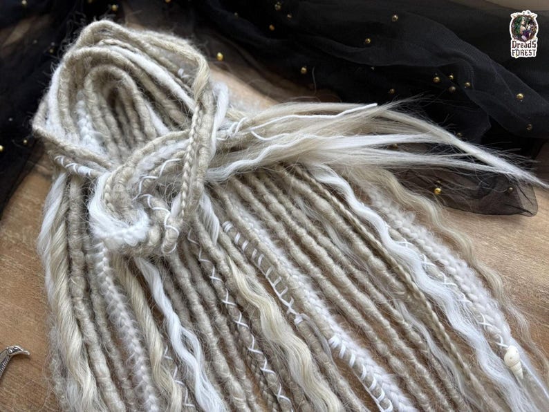 a close-up view of a pile of various colored and styled hair braids or dreadlocks, with a black fabric or sheer material in the background.