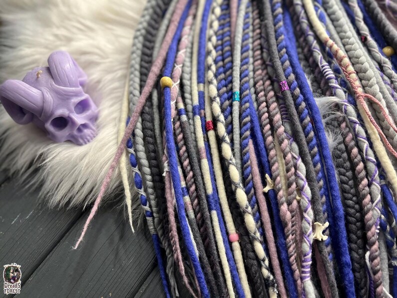 a variety of colorful braided hair accessories, including braids and braided strands, arranged on a wooden surface. There is also a purple skull-shaped object placed next to the hair accessories.