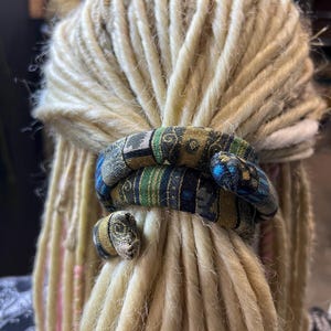 以下が含まれることがあります： カラフルな模様の布製のヘアタイで結ばれたブロンドのドレッドロックのクローズアップ。