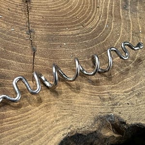 May include: A silver metal hair coil, shaped like a snake, is lying on a wooden surface.