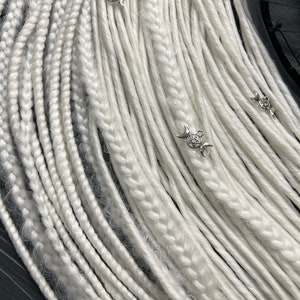 May include: A bundle of white synthetic dreadlocks with silver charms. The charms feature a pentacle and crescent moon design.