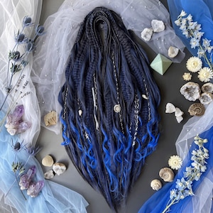 May include: A set of synthetic hair extensions featuring a blend of deep black and dark blue strands that transition into vibrant electric blue tips. The hair is styled with various braids, twists, and silver-toned charms throughout the length.
