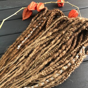 a collection of braided hair strands arranged on a wooden surface, with a few orange dried flowers nearby.