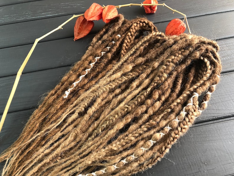 a collection of braided hair strands arranged on a wooden surface, with a few orange dried flowers nearby.