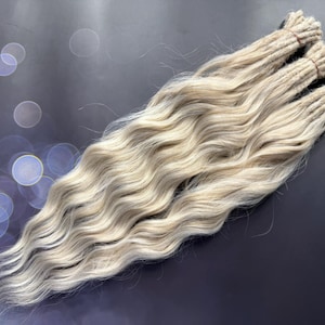May include: Three strands of wavy, light blonde human hair extensions. The hair is tied together with brown string at the top.