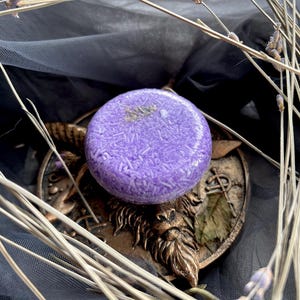 May include: Purple shampoo bar with a glittery texture, sitting on a decorative gold metal stand with a goat head design.