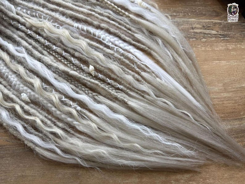 a close-up view of a collection of variously braided and woven hair strands, with a mix of white, gray, and brown colors. The strands appear to be made of yarn or similar materials, and they are arranged in a way that creates a textured and intricate appearance.