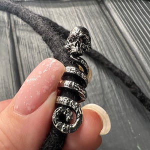 May include: Silver dreadlock bead with a skull design. The bead is shaped like a spiral and has a detailed skull at the top.
