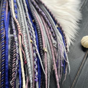 A close-up view of a collection of braided hair accessories in various colors, including blue, purple, and gray, arranged on a wooden surface.