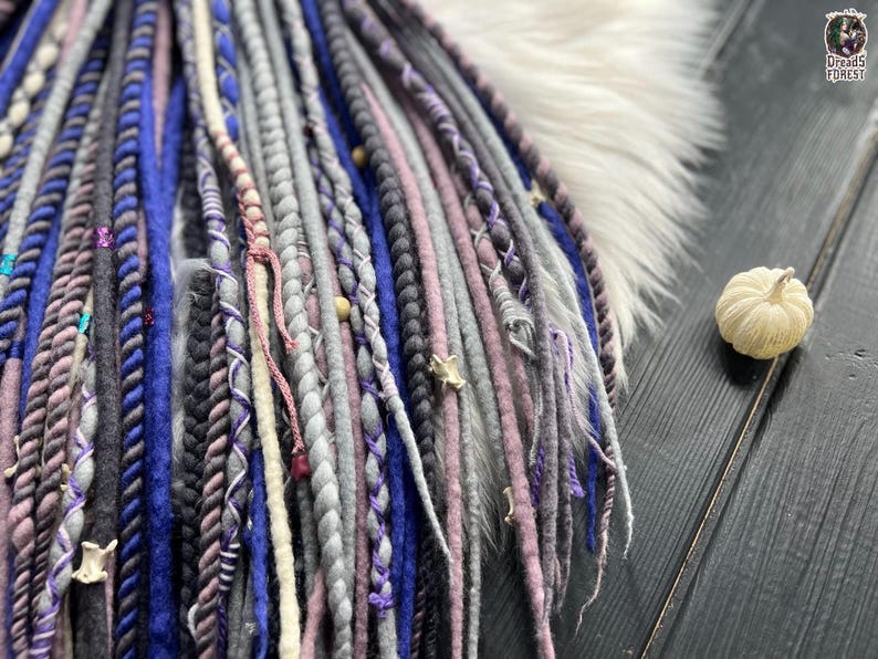 A close-up view of a collection of braided hair accessories in various colors, including blue, purple, and gray, arranged on a wooden surface.