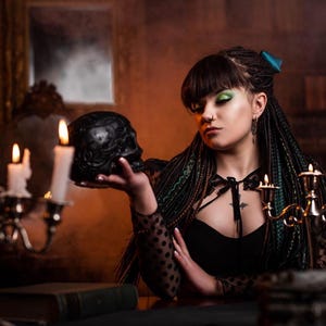Back view of a full set of forest green and black synthetic dreadlocks and braids. The hair is tied with a large teal satin bow, showing how the extensions look from behind. The photo highlights the mix of textures and the natural fall of the long dreads against a dark green smoky background.