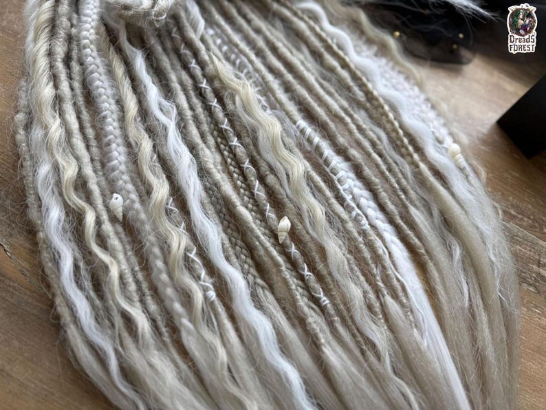 A close-up view of various braided and twisted hair strands in different shades of white and beige, arranged on a wooden surface.