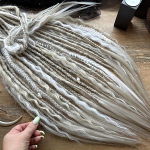 a person's hand holding a bundle of long, white braided hair on a wooden surface.