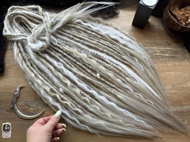 a person's hand holding a bundle of long, white braided hair on a wooden surface.