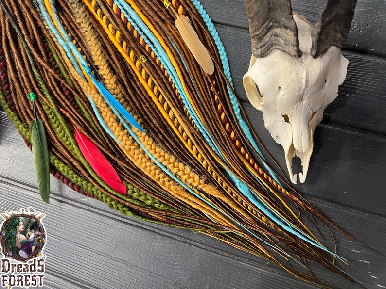 May include: A collection of colorful synthetic dreadlocks in shades of brown, yellow, green, blue, and red. The dreadlocks are arranged in a fan shape and are accented with feathers.