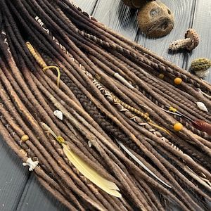May include: Brown and black synthetic dreadlocks with white and gold accents. The dreadlocks are decorated with feathers, beads, and shells.