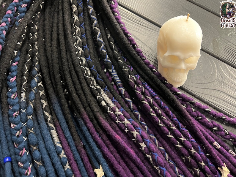 Puede incluir: Una colecci&oacute;n de rastas sint&eacute;ticas en varios tonos de morado, azul y negro. Las rastas est&aacute;n dispuestas en forma de abanico y tienen una variedad de texturas y patrones.