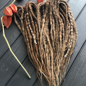 a collection of braided hair strands in various shades of brown, arranged on a wooden surface. There are also red flowers, possibly dried, placed next to the braided hair.