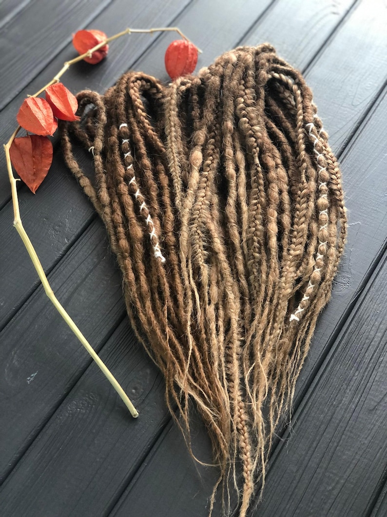 a collection of braided hair strands in various shades of brown, arranged on a wooden surface. There are also red flowers, possibly dried, placed next to the braided hair.