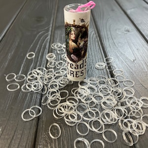 May include: A clear plastic container filled with a large quantity of clear rubber bands. The container has a label that reads "Dread's Forest". The container is sitting on a dark wood surface.