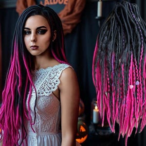 Puede incluir: Una persona con rastas negras y rosas, vestida con un vestido blanco con detalles de encaje. Las rastas están peinadas con negro en las raíces y rosa vibrante en los extremos. La imagen tiene un tema de Halloween con calabazas y velas.