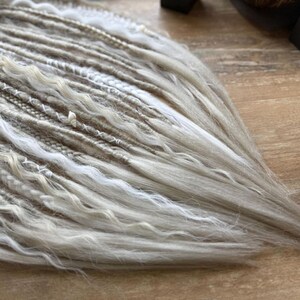 a close-up view of a collection of white and gray braided or woven hair strands arranged on a wooden surface.