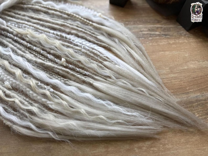 a close-up view of a collection of white and gray braided or woven hair strands arranged on a wooden surface.