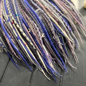 a close-up view of a collection of colorful braided hair accessories, including various shades of blue, purple, and gray braids, arranged on a wooden surface.