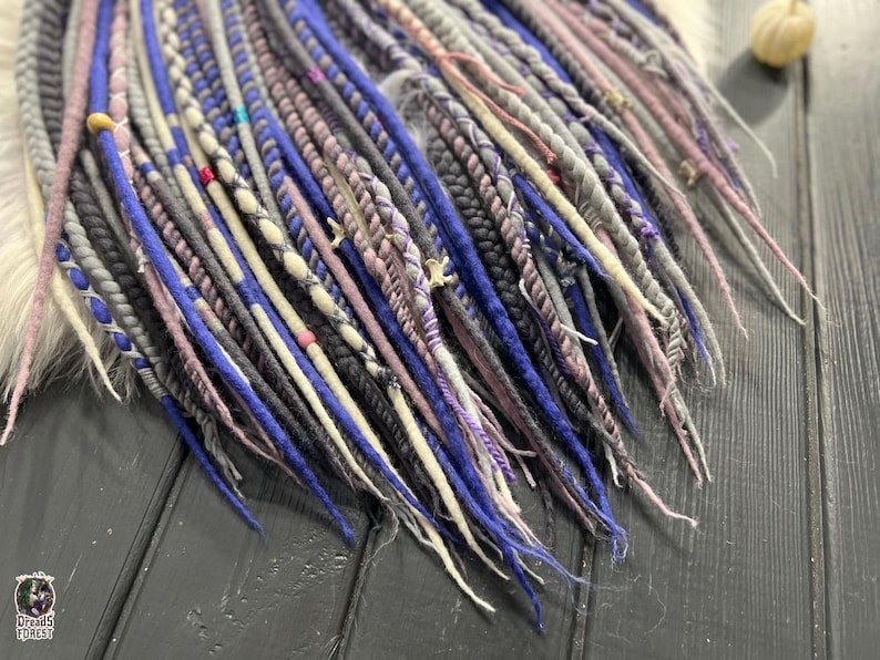 a close-up view of a collection of colorful braided hair accessories, including various shades of blue, purple, and gray braids, arranged on a wooden surface.
