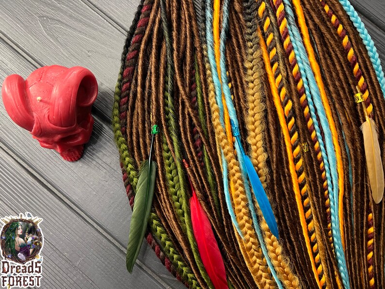 May include: A collection of synthetic dreadlocks in various shades of brown, yellow, red, and blue. The dreadlocks are decorated with feathers and beads.