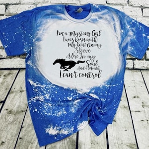 Puede incluir: Una camiseta de color azul y blanco tie-dye con el texto "I'm a Mustang Girl I was born with my heart on my sleeve A fire in my soul And a mouth I can't control" impreso en negro.