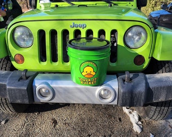 Pode incluir: Um Jeep Wrangler verde com um balde verde com um pato amarelo e o texto "Got Ducked" e "Duck-It Bucket" no para-choques dianteiro.