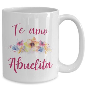 May include: White ceramic mug with a curved handle. The mug features the text "Te amo Abuelita" in a pink script font, along with a watercolor floral design in shades of pink, yellow, and blue.
