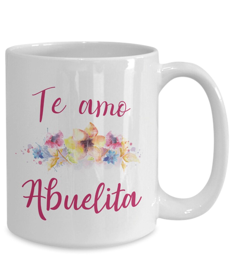 May include: White ceramic mug with a curved handle. The mug features the text "Te amo Abuelita" in a pink script font, along with a watercolor floral design in shades of pink, yellow, and blue.