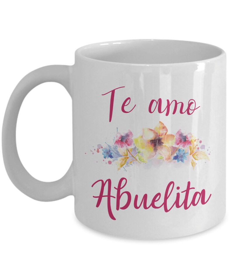 May include: White ceramic mug with a curved handle. The mug features the text "Te amo Abuelita" in pink script, along with a watercolor floral design in shades of pink, yellow, and blue.