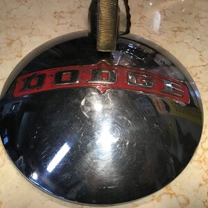 May include: A vintage chrome car hubcap with a red and silver "DODGE" emblem.