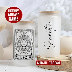 May include: Two frosted glass tumblers with bamboo lids. One tumbler features a black and white illustration of a lion with the word "LEO" below it. The other tumbler has the name "Samantha" written in cursive.  Customize with any name.