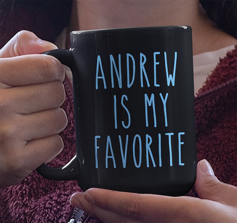 May include: Black coffee mug with a white handle. The mug has blue text that reads "ANDREW IS MY FAVORITE".
